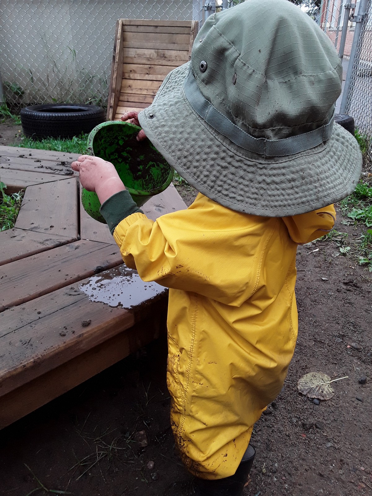Child in rainsuit playing with mud in a bucket