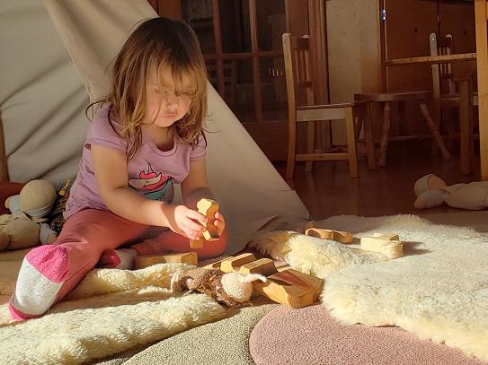 Child playing with wooden toys on the floor, soft fur rugs and blankets